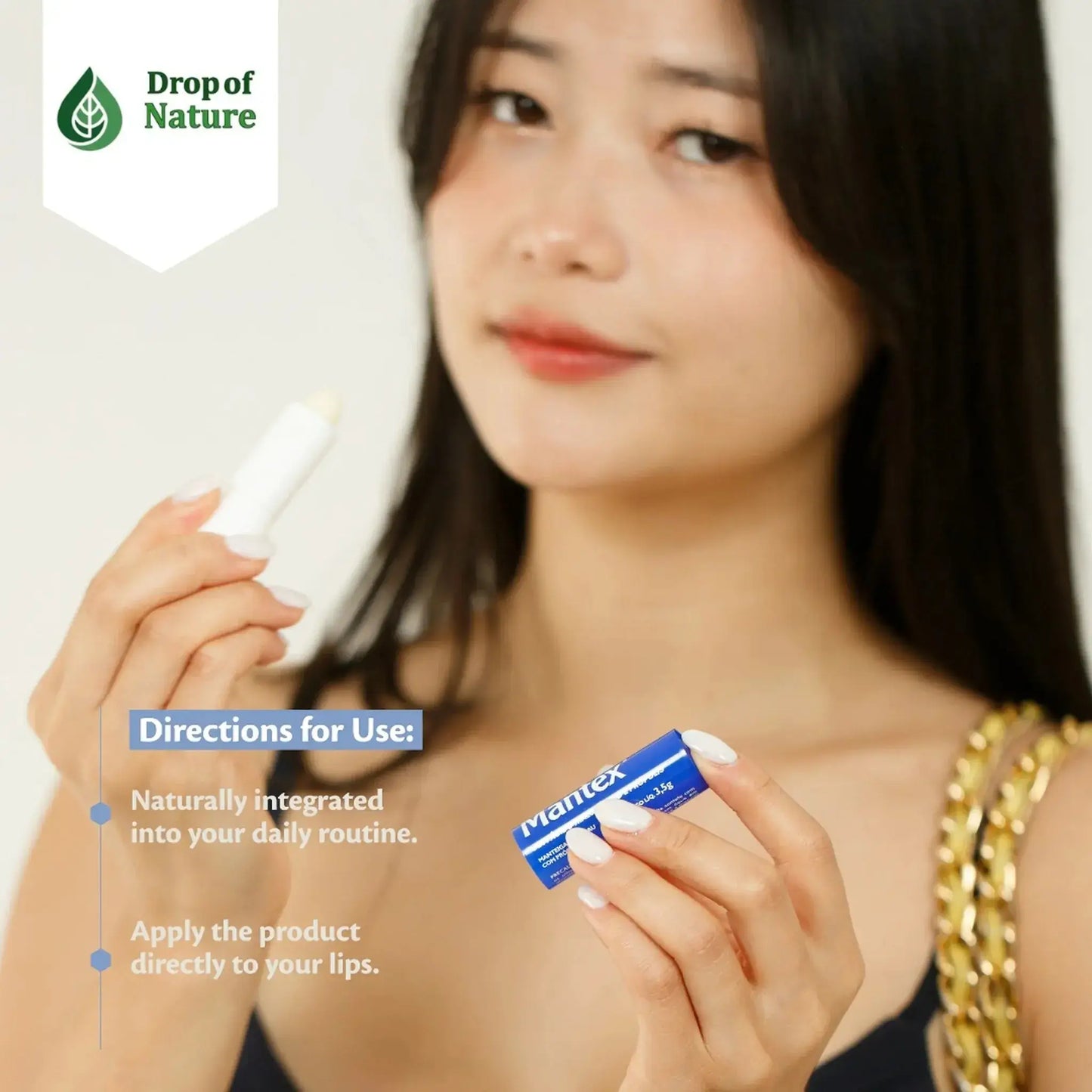 A person holds a white lip balm tube with a blue label, smiling and wearing a casual outfit.