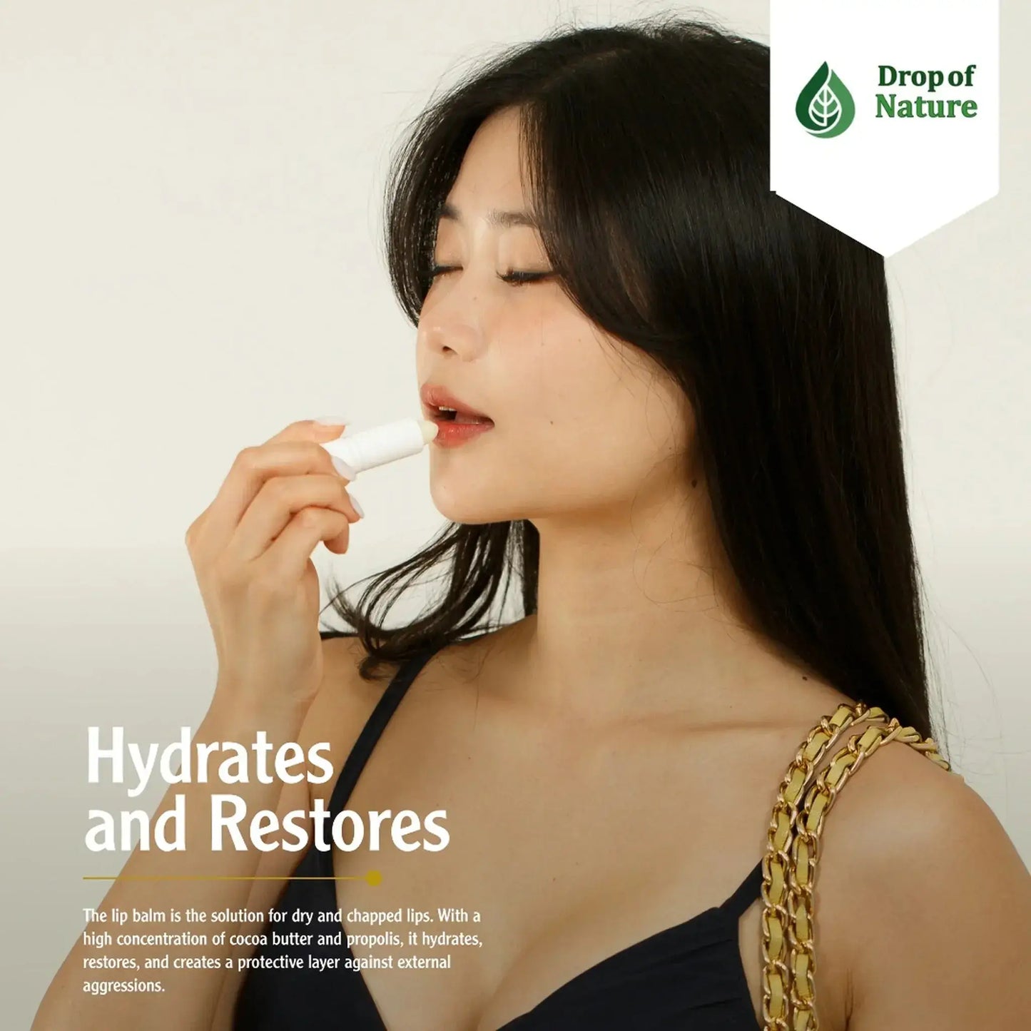 Woman applying lip balm while looking to the side, wearing a black top and holding a handbag; product labeled Drop of Nature.