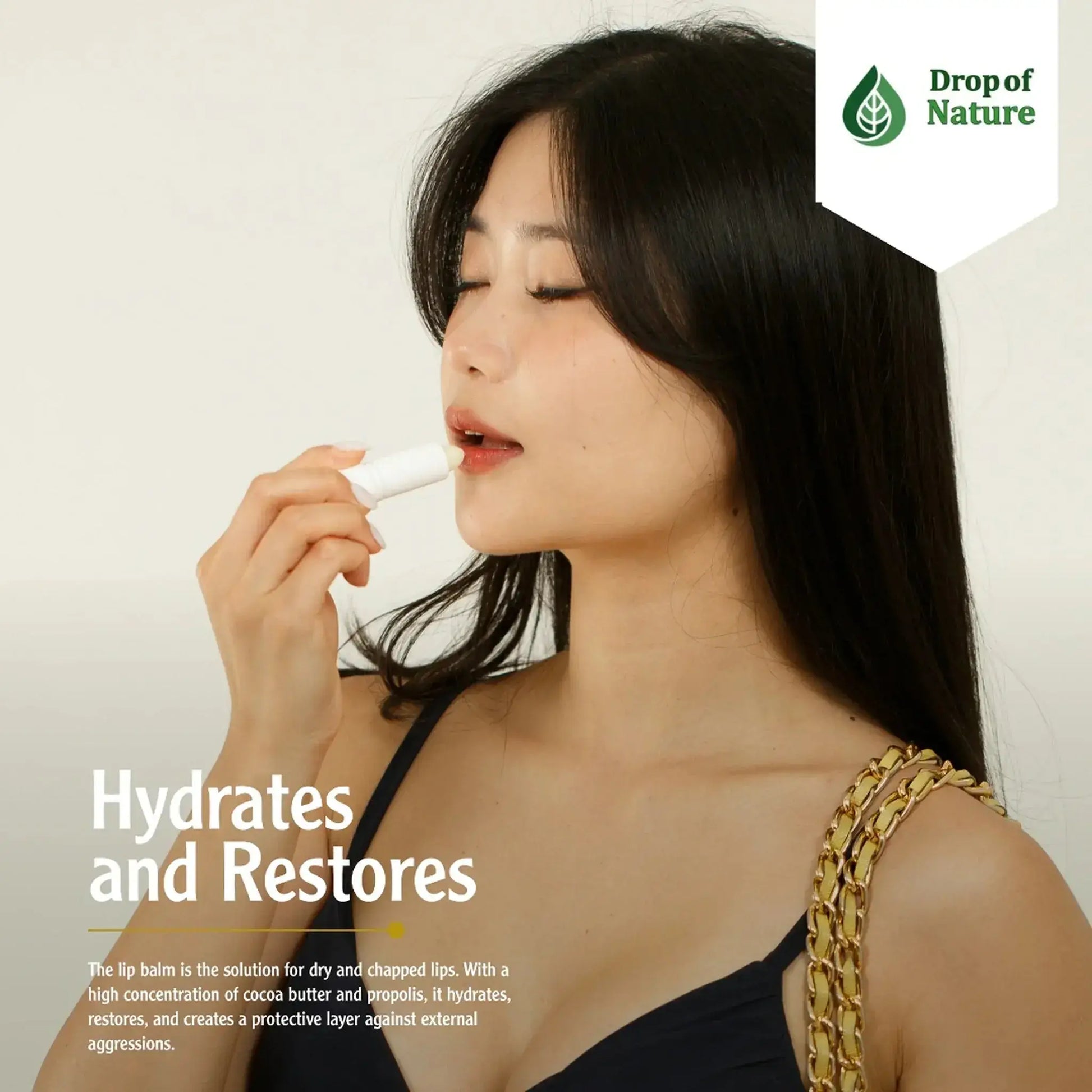 Woman applying lip balm while looking to the side, wearing a black top and holding a handbag; product labeled Drop of Nature.
